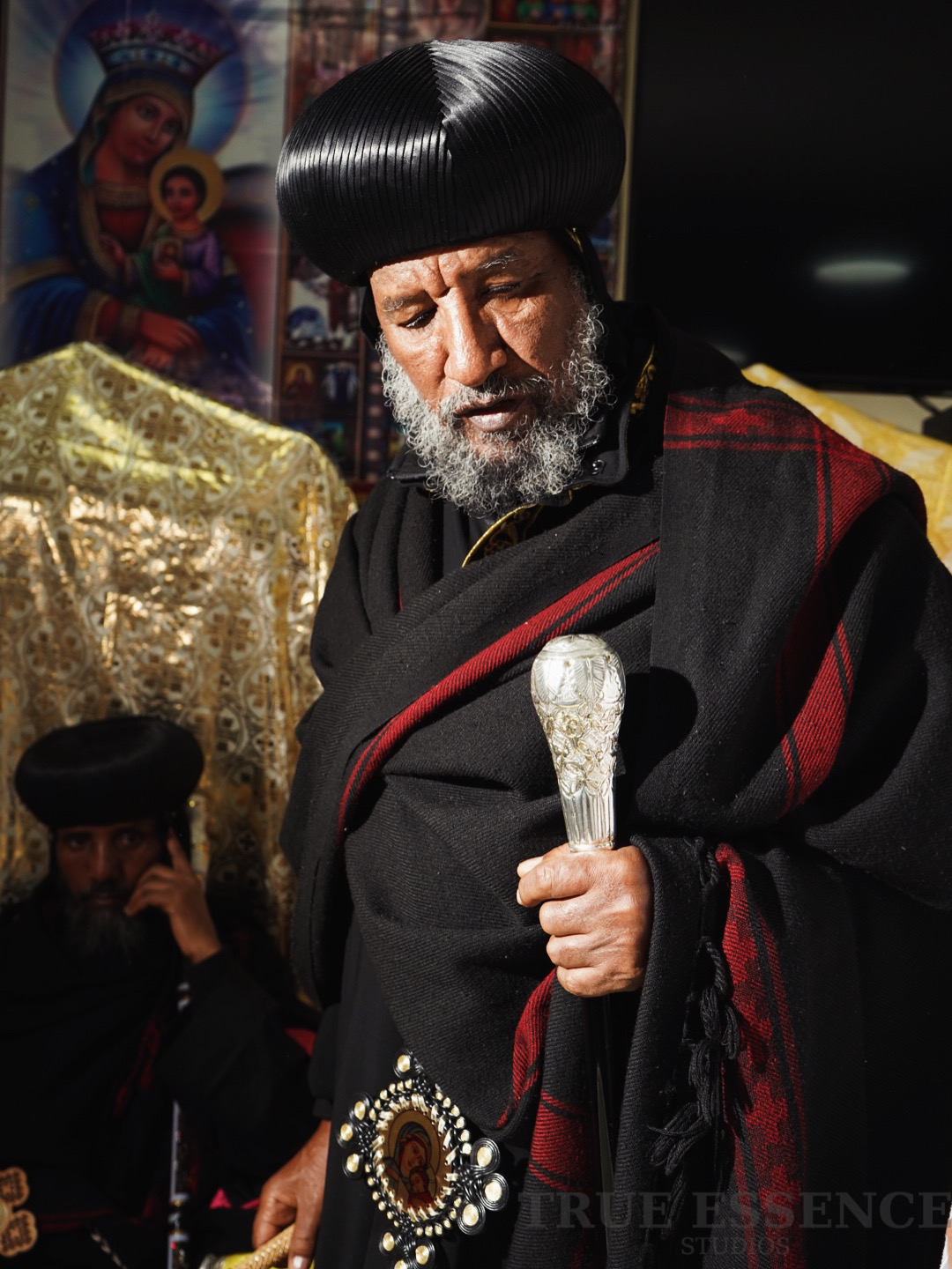 Geistlicher der Eritreisch-Orthodoxen Tewahedo Kirche im schwarzen Gewand mit Segensstab vor Ikonen